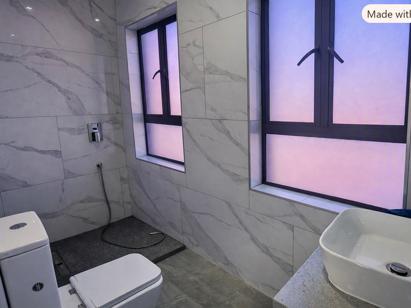 Modern bathroom featuring marble-look wall tiles, dual-pane windows, a vessel sink on a stone vanity, and a wall-mounted bidet sprayer.