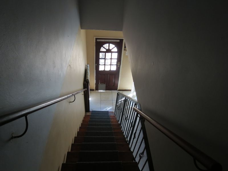 A view looking down a staircase towards the front entrance, featuring a timber door, wrought iron balustrade, and tiled landing area.