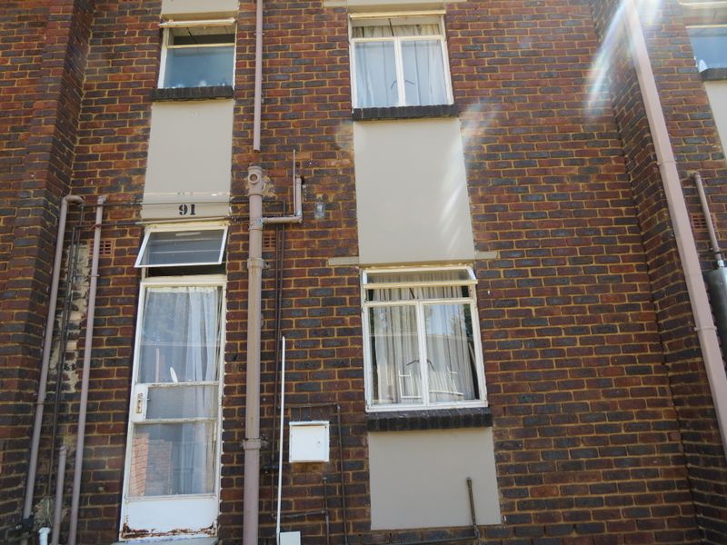 Rear exterior view of a brick townhouse featuring multiple windows, external plumbing, and a security screen door entrance.