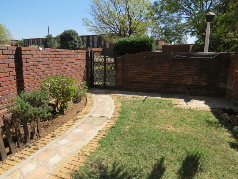 A private rear garden featuring a brick boundary wall, a metal pedestrian gate, a paved walkway, and a small lawn area.
