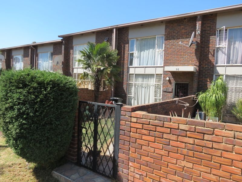 Front exterior view of a face brick townhouse featuring a private courtyard, metal security gate, and established garden area.