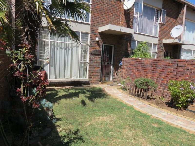 Front exterior view of a brick townhouse featuring a private garden, paved walkway, and secure entrance gate.