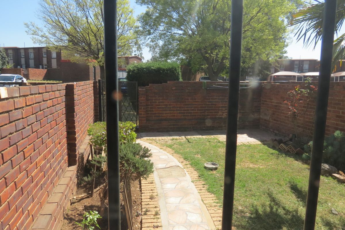 A private rear garden featuring a brick boundary wall, a paved walkway, and a small lawn area, viewed through security bars.