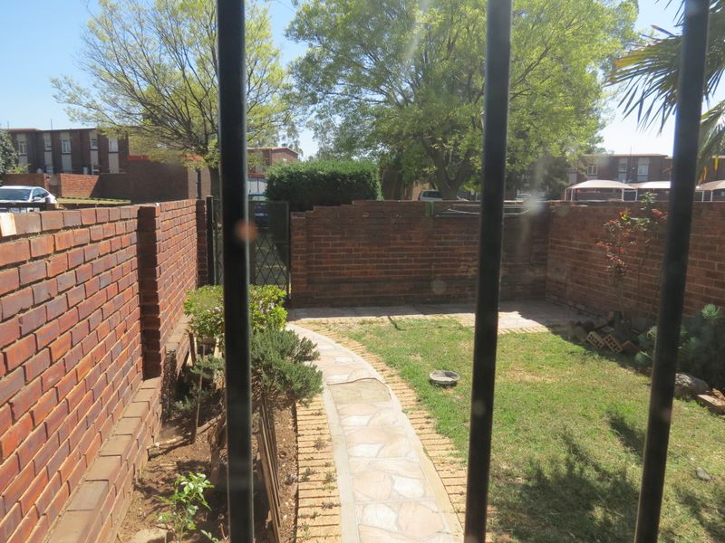 A private rear garden featuring a brick boundary wall, a paved walkway, and a small lawn area, viewed through security bars.