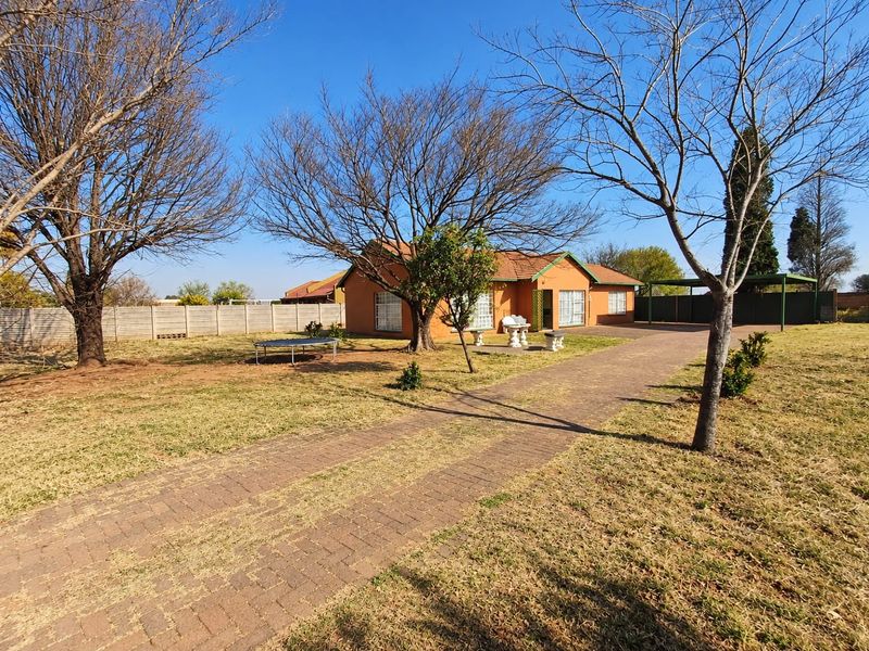 Front view of a single-story house featuring a long paved driveway, precast boundary walling, and a carport on a spacious plot.