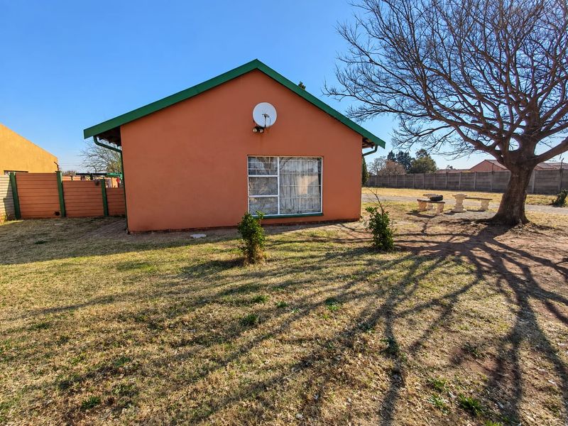 Rear view of the property featuring a simple facade, satellite dish, and a spacious garden area with a large mature tree.
