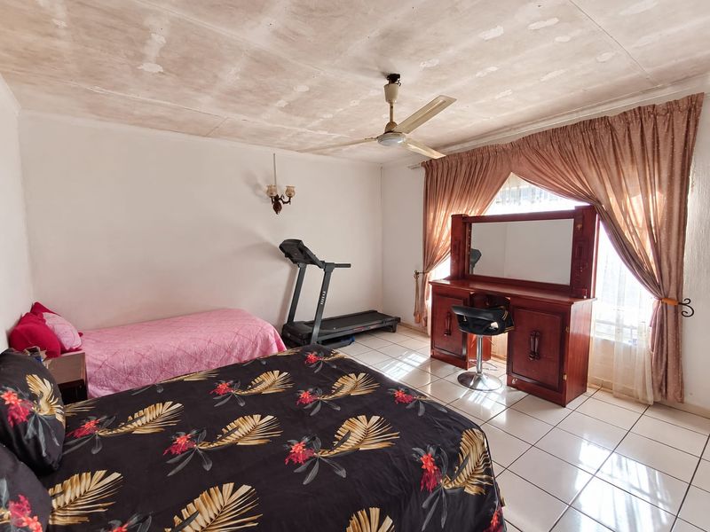 A bedroom featuring tiled flooring, a ceiling fan, and a wall-mounted light fixture, with visible signs of wear on the ceiling surface.