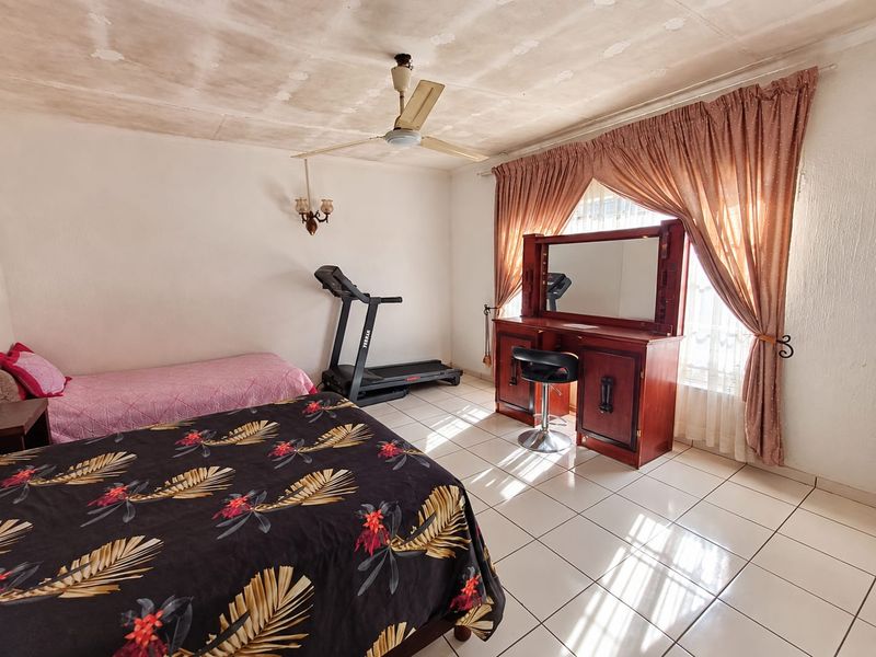 Spacious bedroom featuring tiled flooring, a ceiling fan, and wall-mounted lighting, requiring cosmetic updates to the ceiling finishes.
