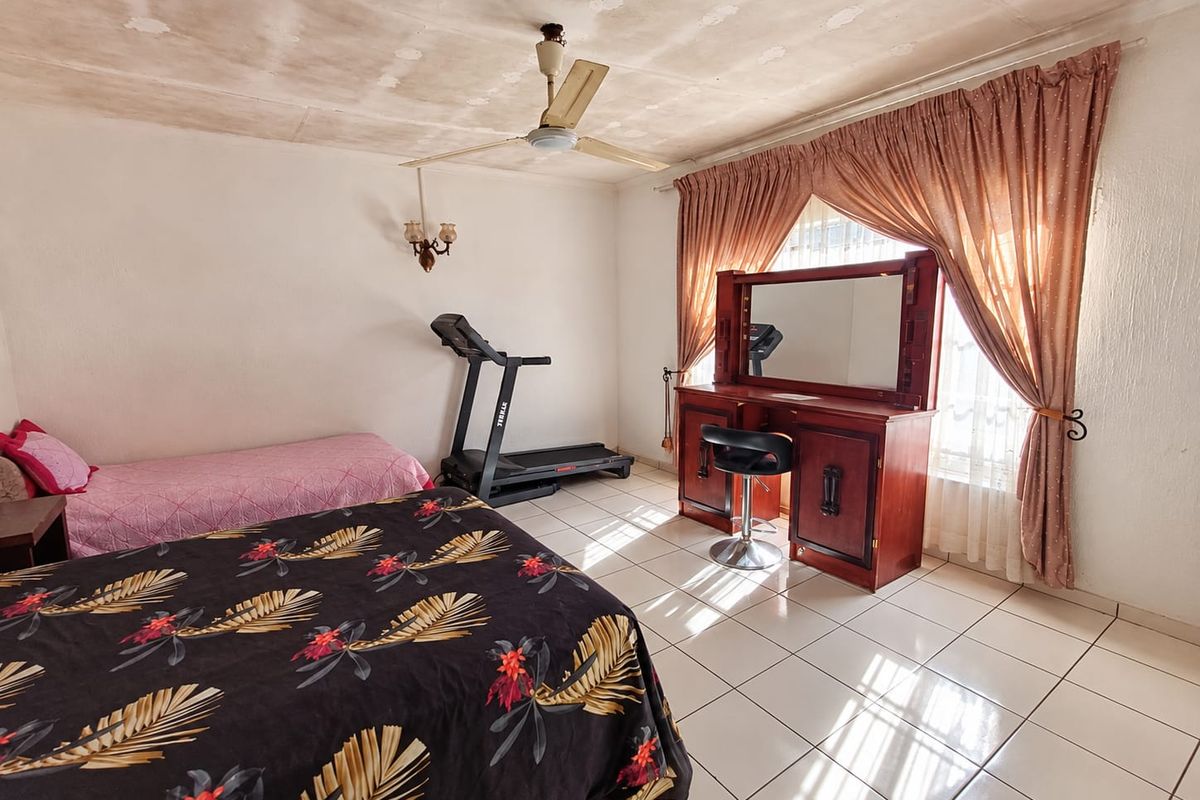 Spacious bedroom featuring tiled flooring, a ceiling fan, and wall-mounted lighting, requiring cosmetic updates to the ceiling finishes.
