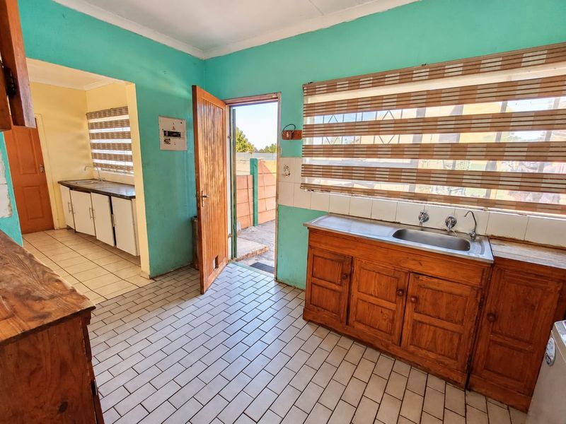Functional scullery area featuring wooden cabinetry, stainless steel sink, tiled flooring, and direct access to the exterior.