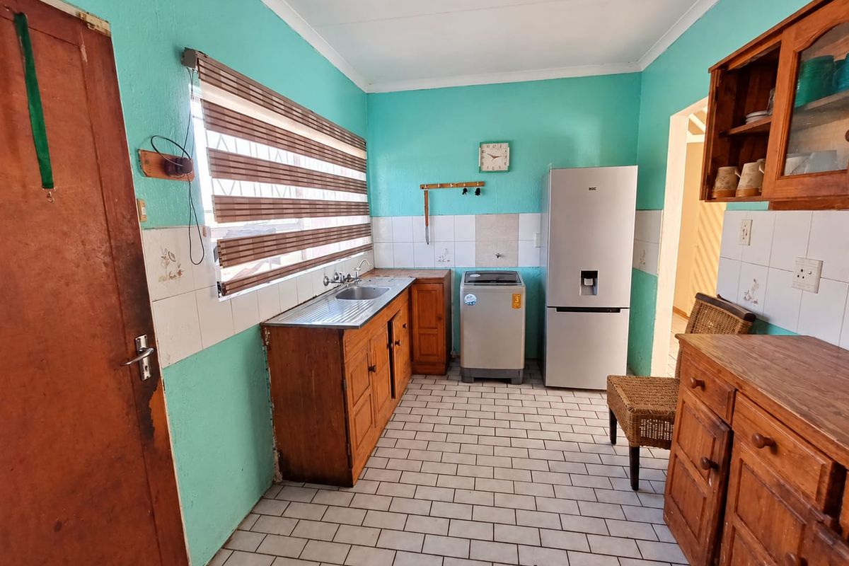 A functional kitchen featuring wooden cabinetry, tiled splashbacks, and tiled flooring, offering a practical layout with space for essential appliances.