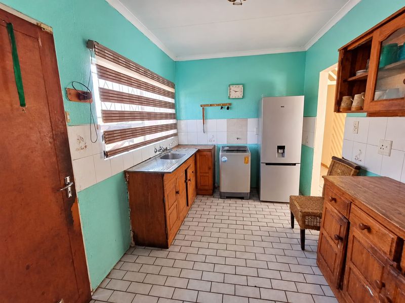 A functional kitchen featuring wooden cabinetry, tiled splashbacks, and tiled flooring, offering a practical layout with space for essential appliances.