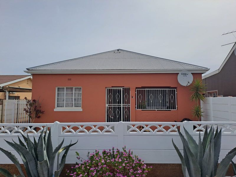 Front elevation of a single-story house featuring a corrugated metal roof, security gates, and a white precast concrete boundary wall.