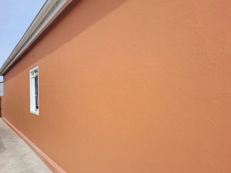 A side view of the property showing a well-maintained plastered exterior wall, white guttering, and a window with security bars.