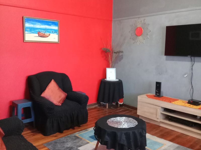 A living room featuring hardwood flooring and a traditional picture rail, currently styled with bold red and grey accent walls.