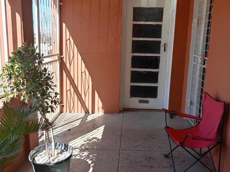 A covered patio area featuring tiled flooring and security gates, providing a functional outdoor entrance space.