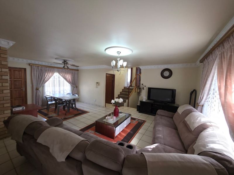 Spacious open-plan living and dining area featuring ceramic tiled flooring, decorative ceiling cornices, and a staircase leading to the upper level.