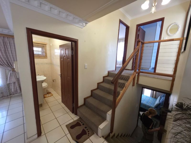 A multi-level hallway featuring a carpeted staircase with wooden handrails, crown molding, and access to a tiled bathroom and adjacent rooms.