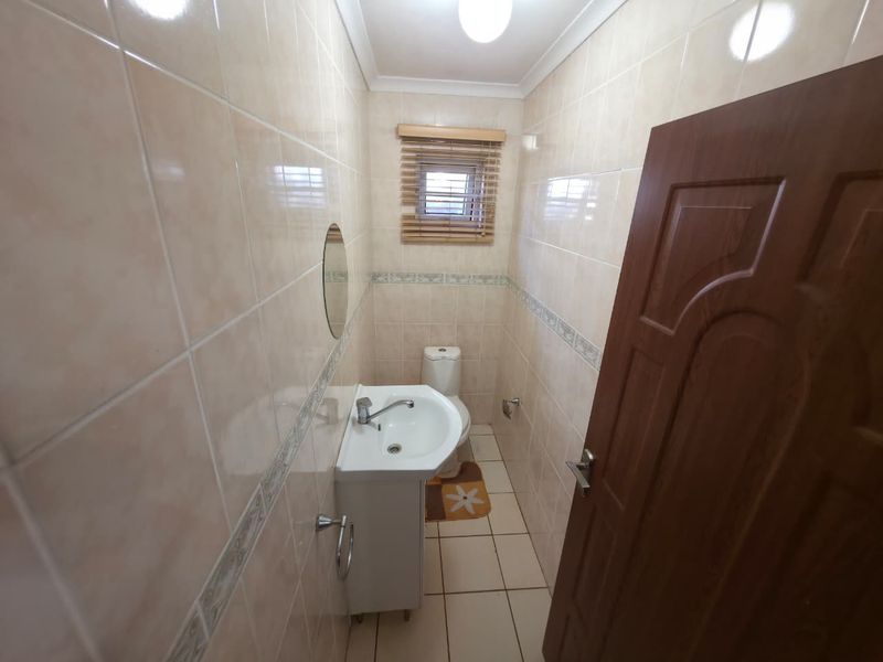 A compact guest bathroom featuring neutral ceramic wall and floor tiles, a pedestal basin, and a toilet.