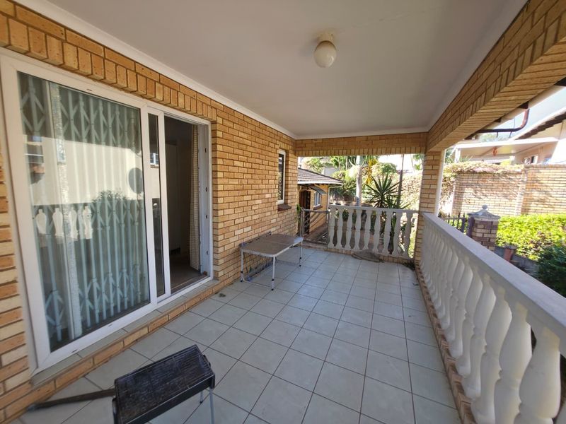 A covered patio area featuring tiled flooring, brick walls, and a classic concrete balustrade, providing a functional outdoor space for relaxation.