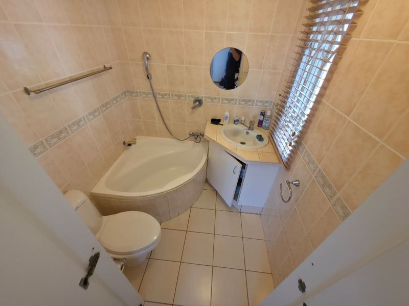 Compact bathroom featuring a corner bathtub, vanity unit with integrated basin, toilet, and full-height wall tiling.