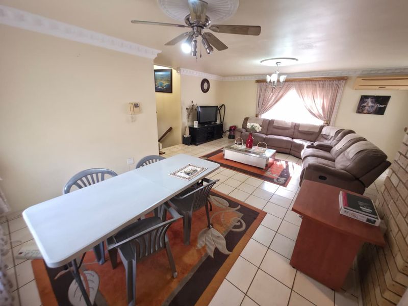 Spacious open-plan living and dining area featuring tiled flooring, ceiling fans, decorative coving, and a brick fireplace.