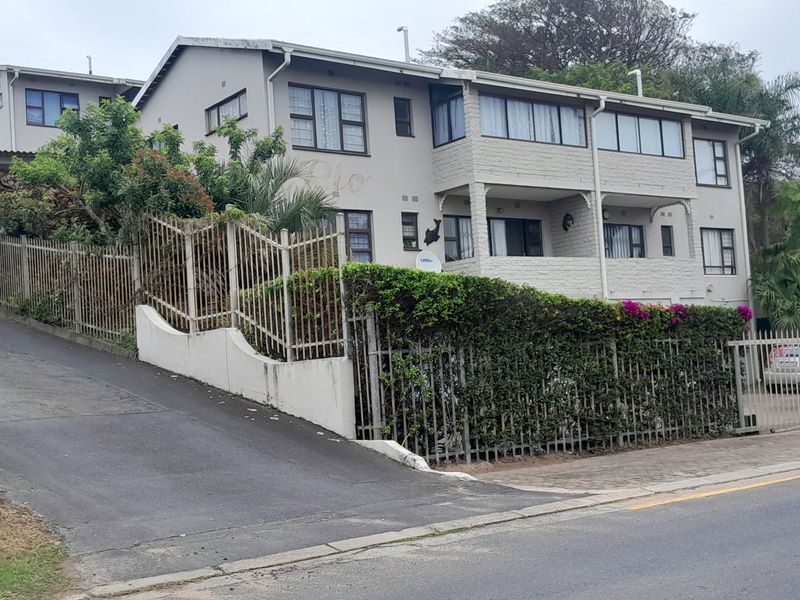Street view of a multi-story apartment complex featuring a paved driveway, secure metal fencing, and balcony access.