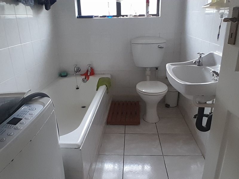 A compact bathroom featuring a bathtub, pedestal basin, and toilet with white wall tiling and floor tiles.