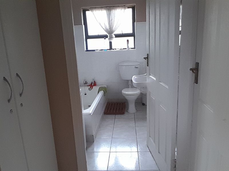 A functional bathroom featuring a bathtub, pedestal basin, and toilet, with tiled flooring and built-in storage cupboards in the adjacent hallway area.