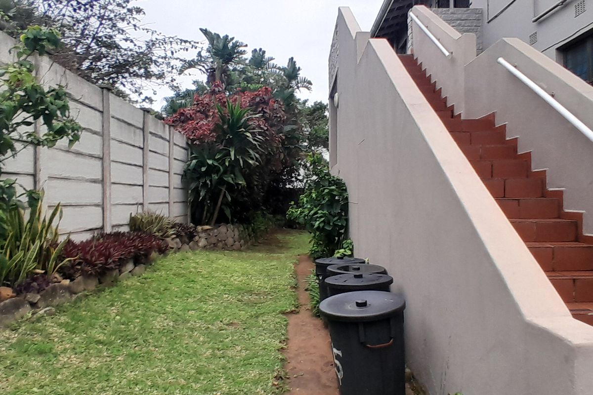 Rear exterior view of the apartment building featuring a private garden area and an external staircase with tiled steps and a handrail.