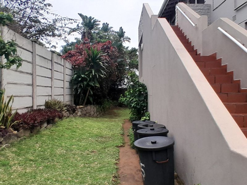 Rear exterior view of the apartment building featuring a private garden area and an external staircase with tiled steps and a handrail.