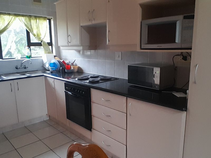 A functional kitchen featuring built-in cabinetry, black granite countertops, an electric hob, built-in oven, and tiled flooring with a tiled backsplash.