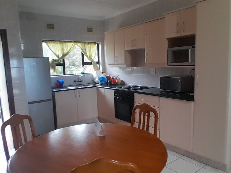 A functional kitchen featuring built-in cabinetry, laminate countertops, an integrated oven and hob, and tiled splashbacks, with direct access to an outdoor area.