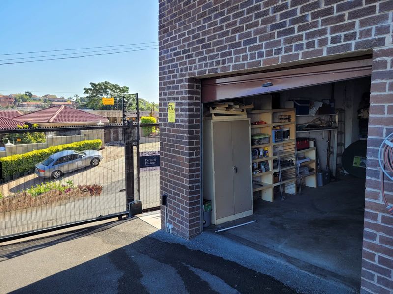 A view of a brick garage entrance with built-in shelving and an adjacent metal security gate leading to the driveway.