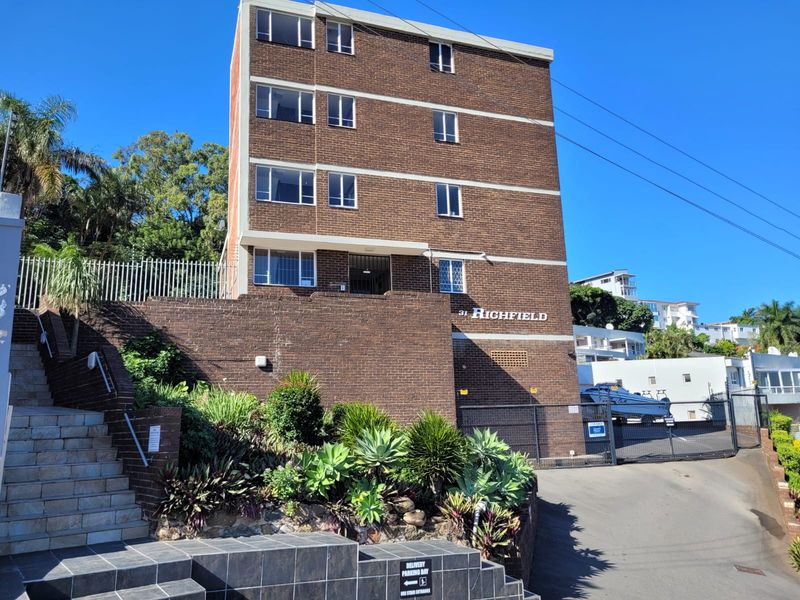Front elevation of the Highfield apartment building featuring a brick facade, landscaped retaining walls, and a paved entrance staircase.