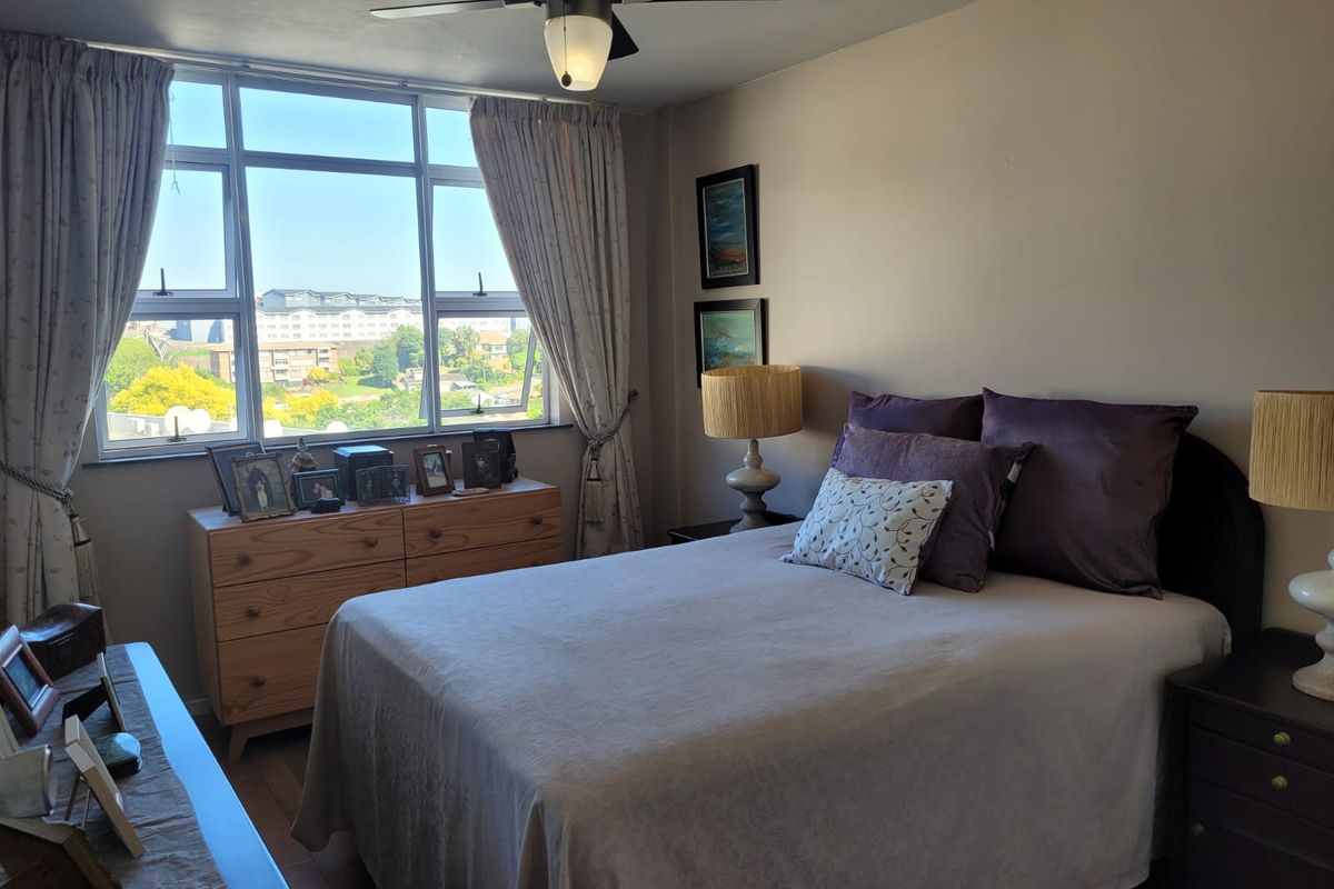 A well-lit bedroom featuring a large window with natural light, a ceiling fan, and laminate flooring, offering a comfortable and functional living space.