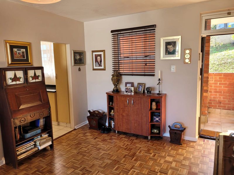 A living room featuring classic parquet flooring, a window with venetian blinds, and direct access to an outdoor area.