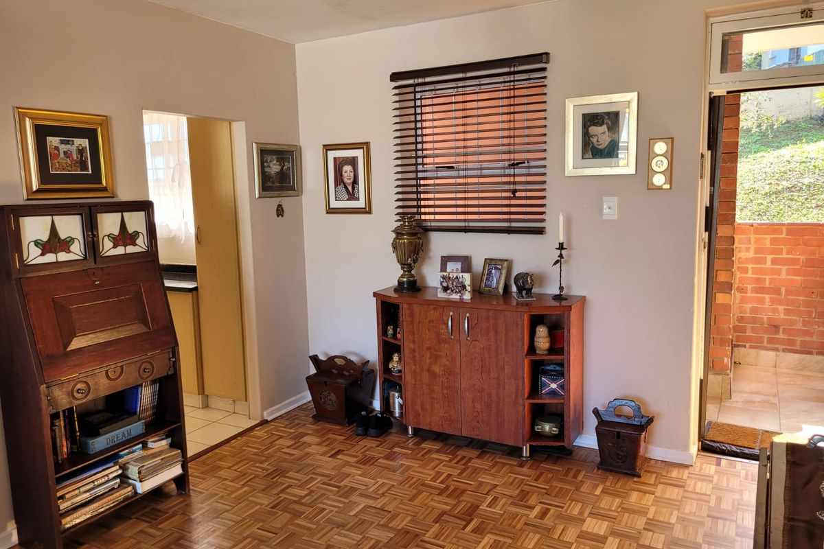 A living room featuring classic parquet flooring, a window with venetian blinds, and direct access to an outdoor area.