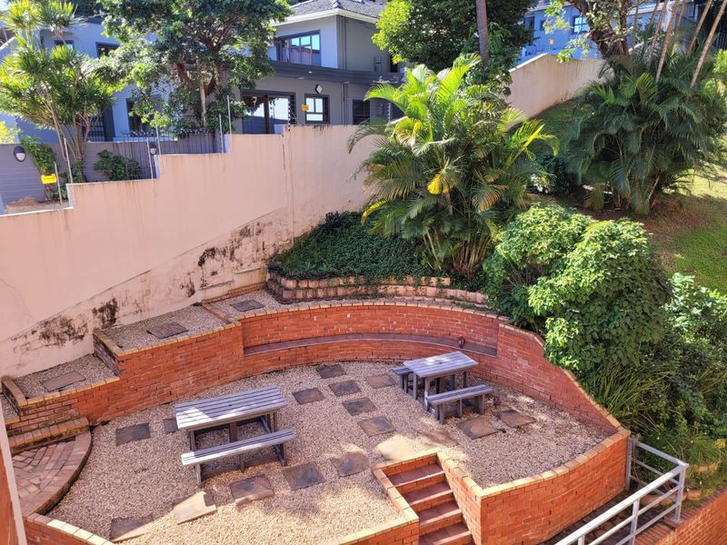 A terraced rear garden area featuring brick retaining walls, built-in brick seating, and a gravel courtyard with paved stepping stones.