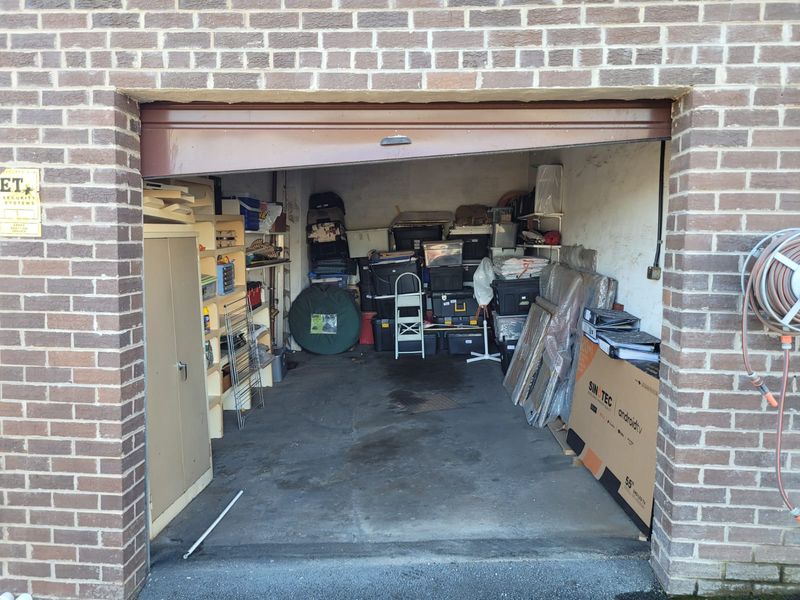 A single-car garage featuring a brick exterior facade and a concrete floor, currently used for storage.