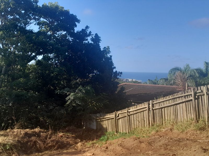 A view of the coastal landscape and surrounding greenery from the vacant residential property, featuring a wooden perimeter fence.