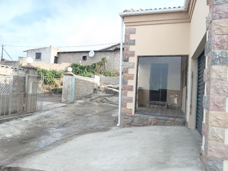 Front exterior view of the property featuring stone cladding accents, a concrete driveway, and gated entrance with perimeter boundary walls.