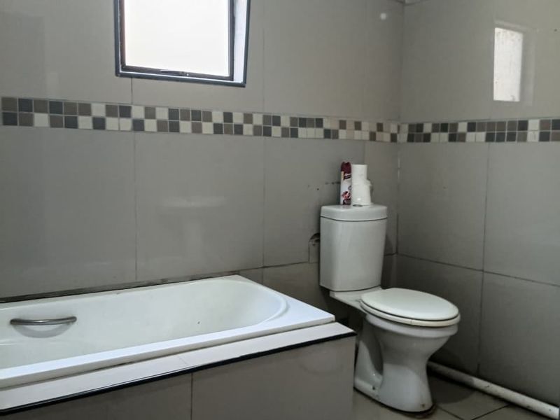 A functional bathroom featuring a built-in bathtub, toilet, and neutral wall and floor tiling with a decorative border.