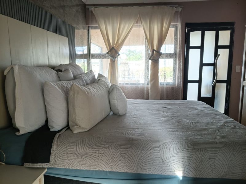 A bedroom featuring a built-in headboard with slatted wall paneling, large aluminium-framed windows, and a modern frosted glass door.