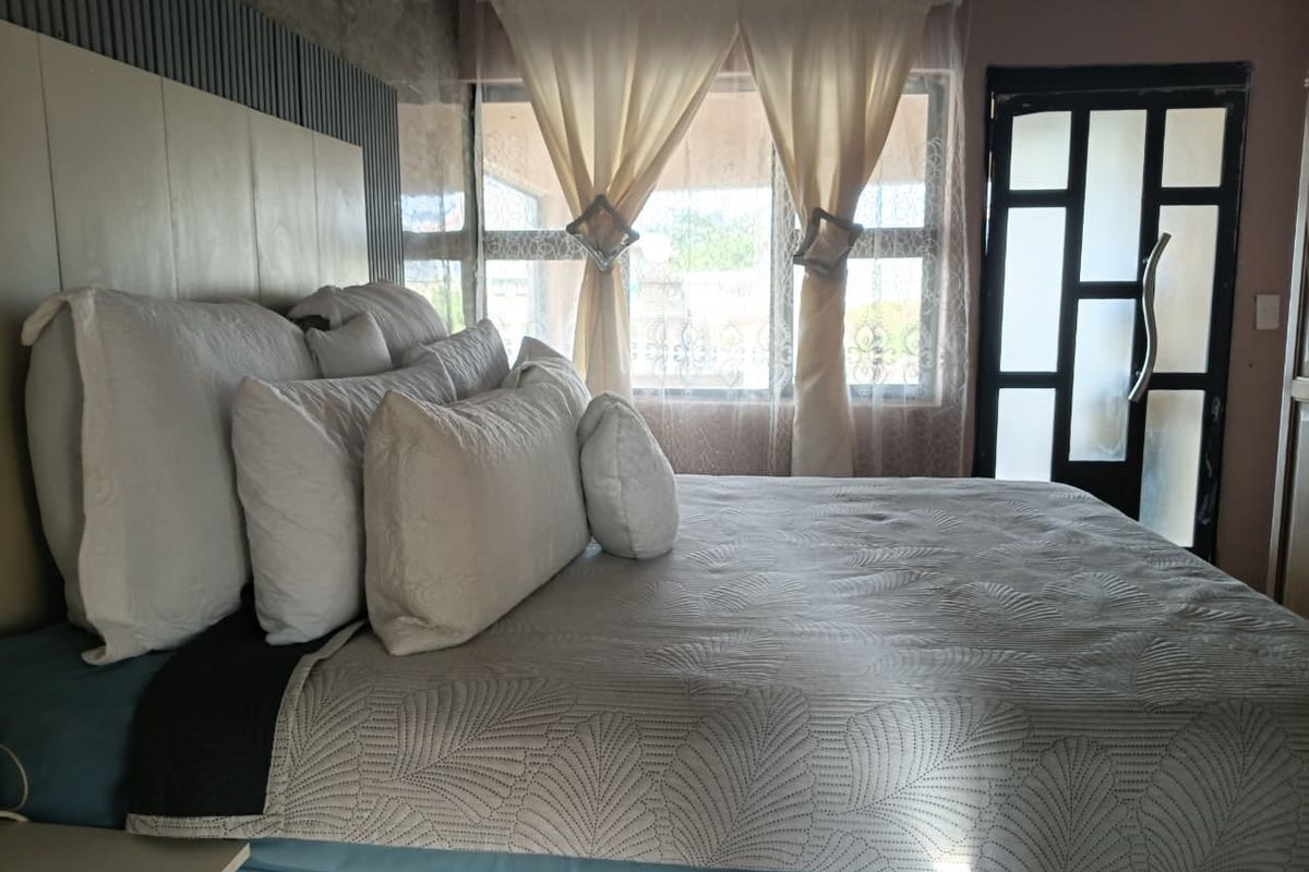 A bedroom featuring a built-in headboard with slatted wall paneling, large aluminium-framed windows, and a modern frosted glass door.