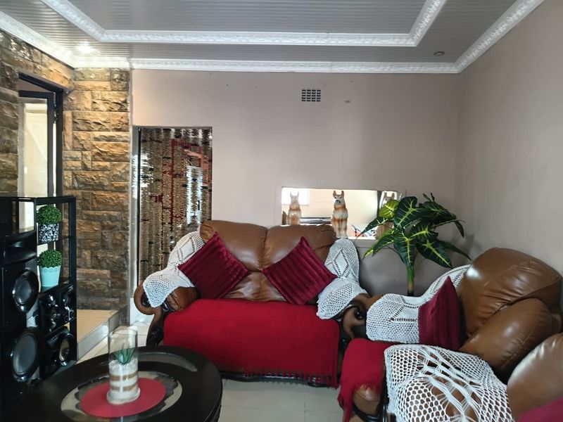 A living room featuring a stone accent wall, decorative coffered ceiling with crown molding, and a convenient pass-through window to the adjacent space.
