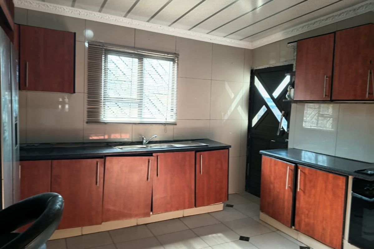 A functional kitchen featuring wood-look cabinetry, dark countertops, tiled backsplash, and built-in oven, with direct access to an exterior door.