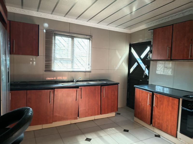 A functional kitchen featuring wood-look cabinetry, dark countertops, tiled backsplash, and built-in oven, with direct access to an exterior door.