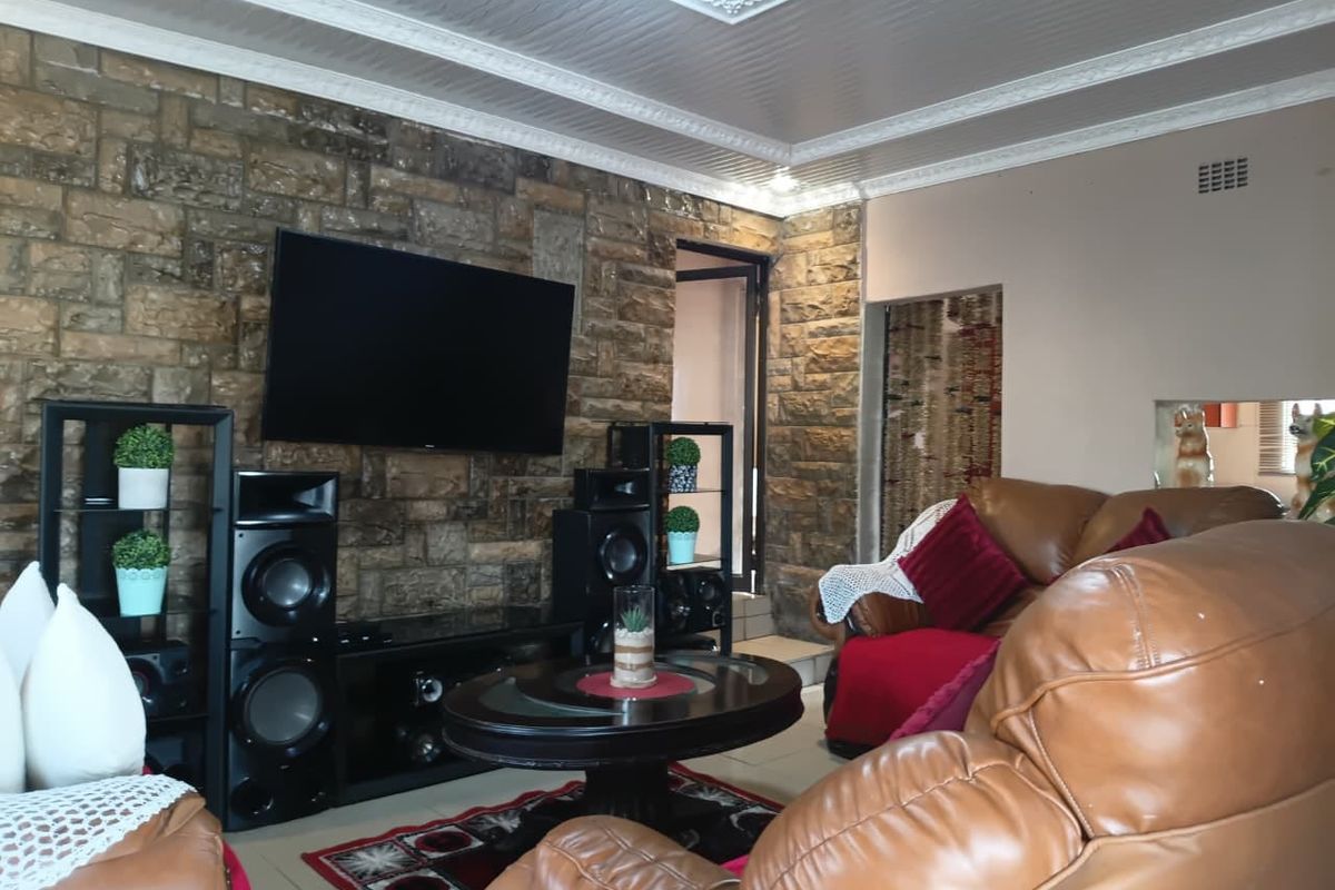 A living room featuring a prominent stone accent wall, decorative ceiling molding, and tiled flooring.