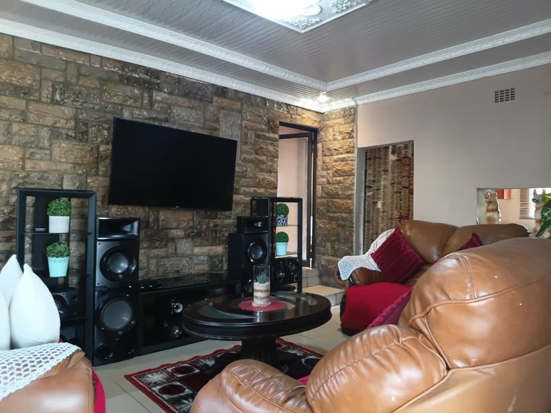 A living room featuring a prominent stone accent wall, decorative ceiling molding, and tiled flooring.